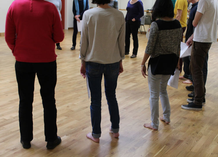 Un groupe de personne se tient debout, en cercle, dans une salle. On ne voit pas leurs visages.