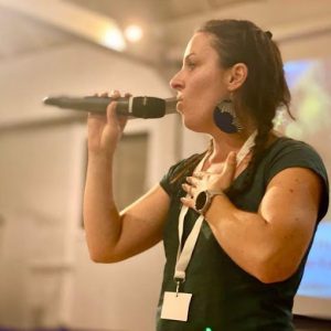 unnamed Celine Dahan se tient debout de profil dans une pièce avec un un micro dans sa main droite, qu'elle porte auprès de sa bouche.